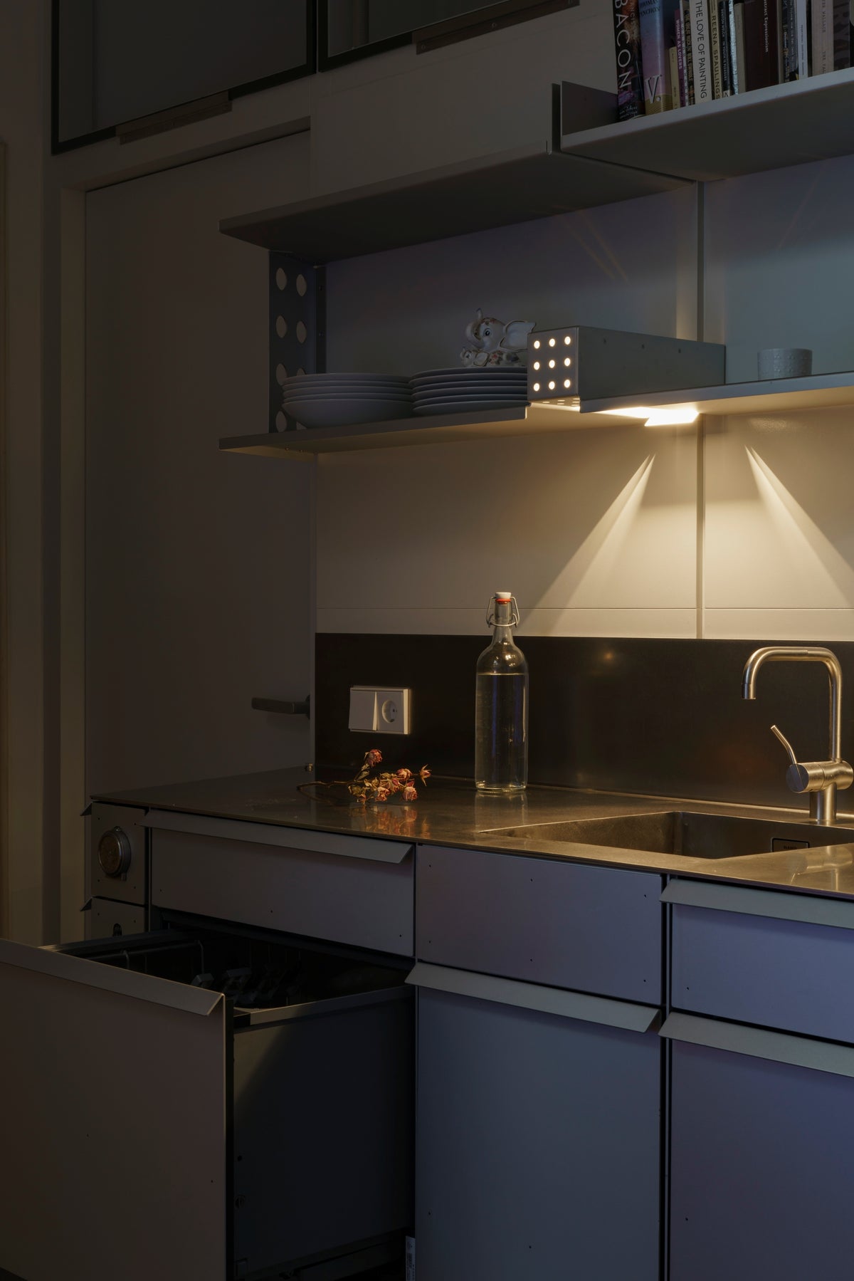 Sink end of the kitchen with one shelf light on above the splashback and a lower drawer pulled open