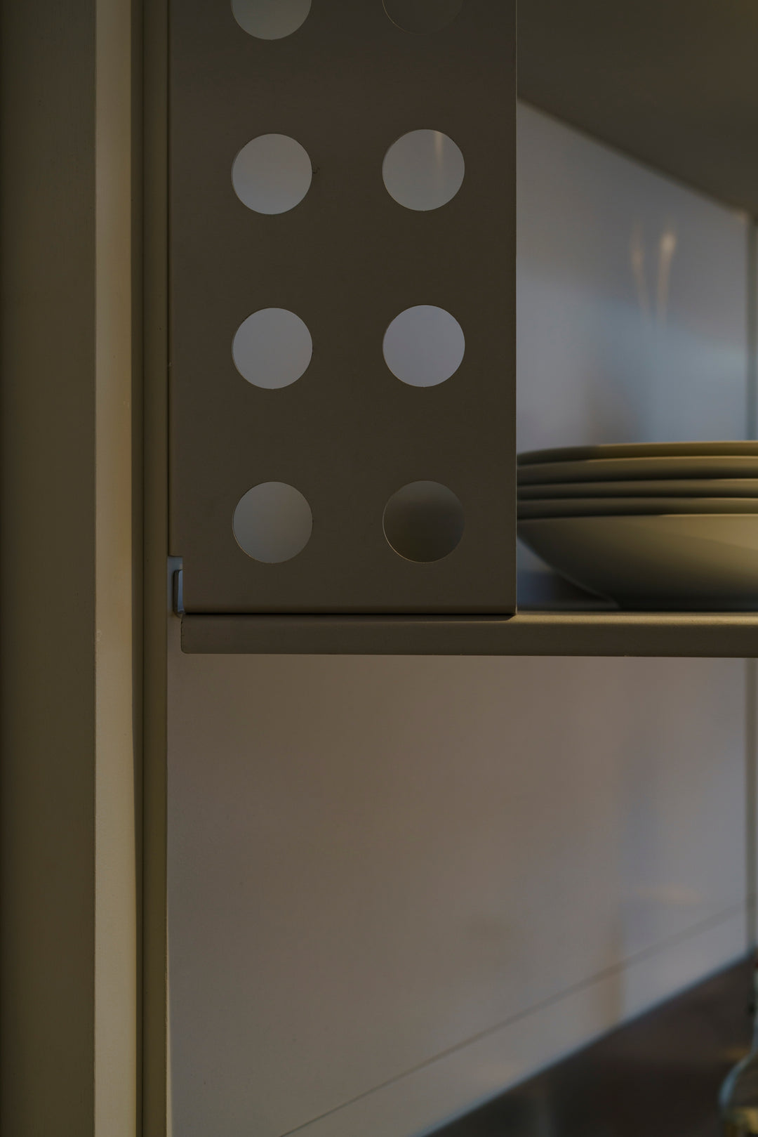 Perforated anodised aluminium shelf bracket beside stacked plates on an open kitchen shelf