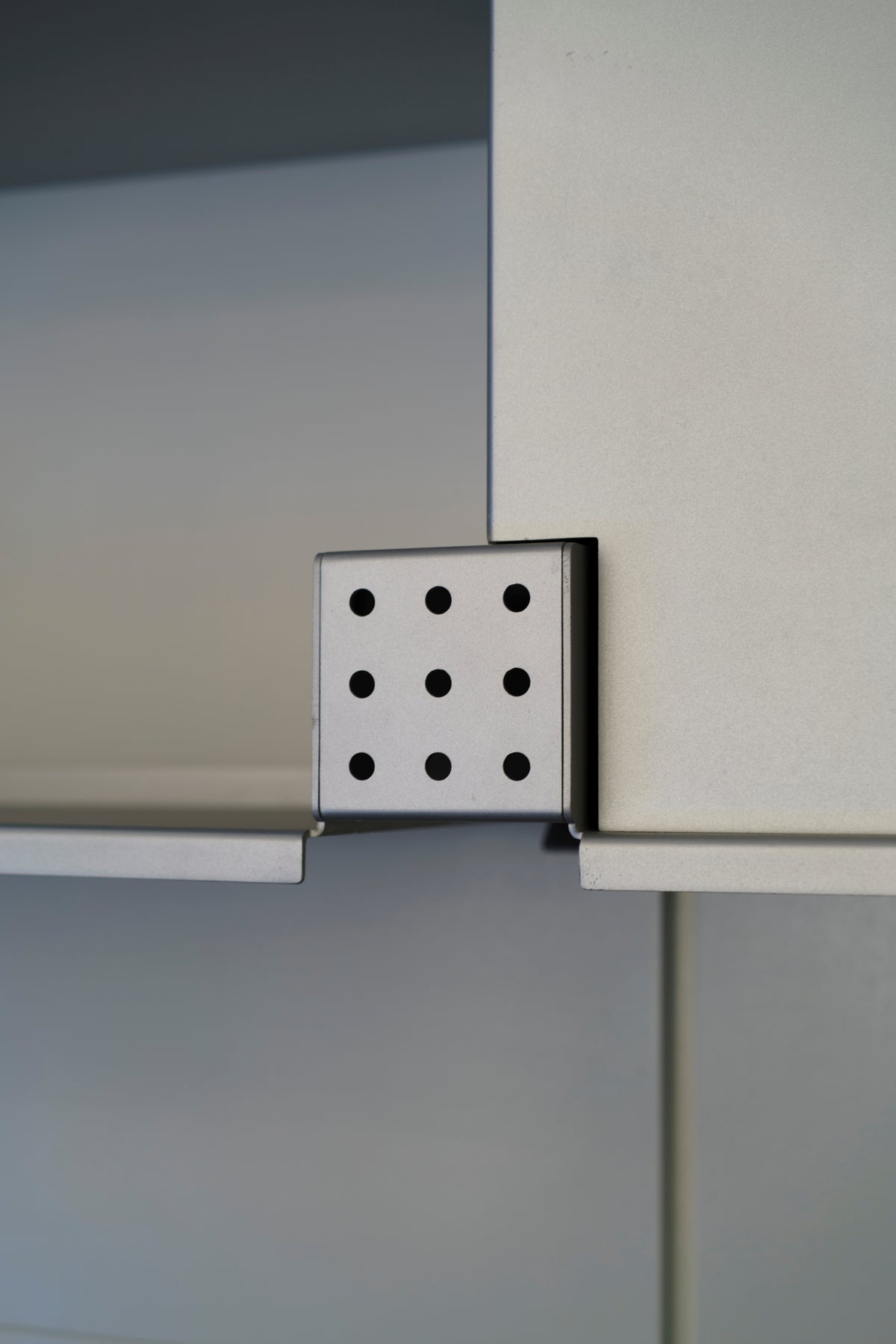 The nine-hole shelf light unlit in daylight, its anodised aluminium body bracketed between two shelves